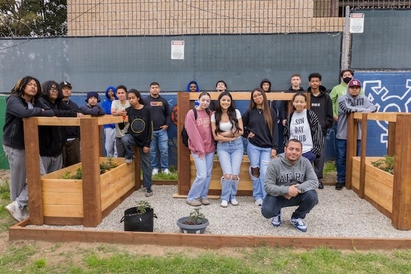 Large group of IVA students in front of raised gardening beds in backyard