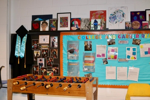 Foosball table  in front of wall with bulletin board with colorful posters on it.