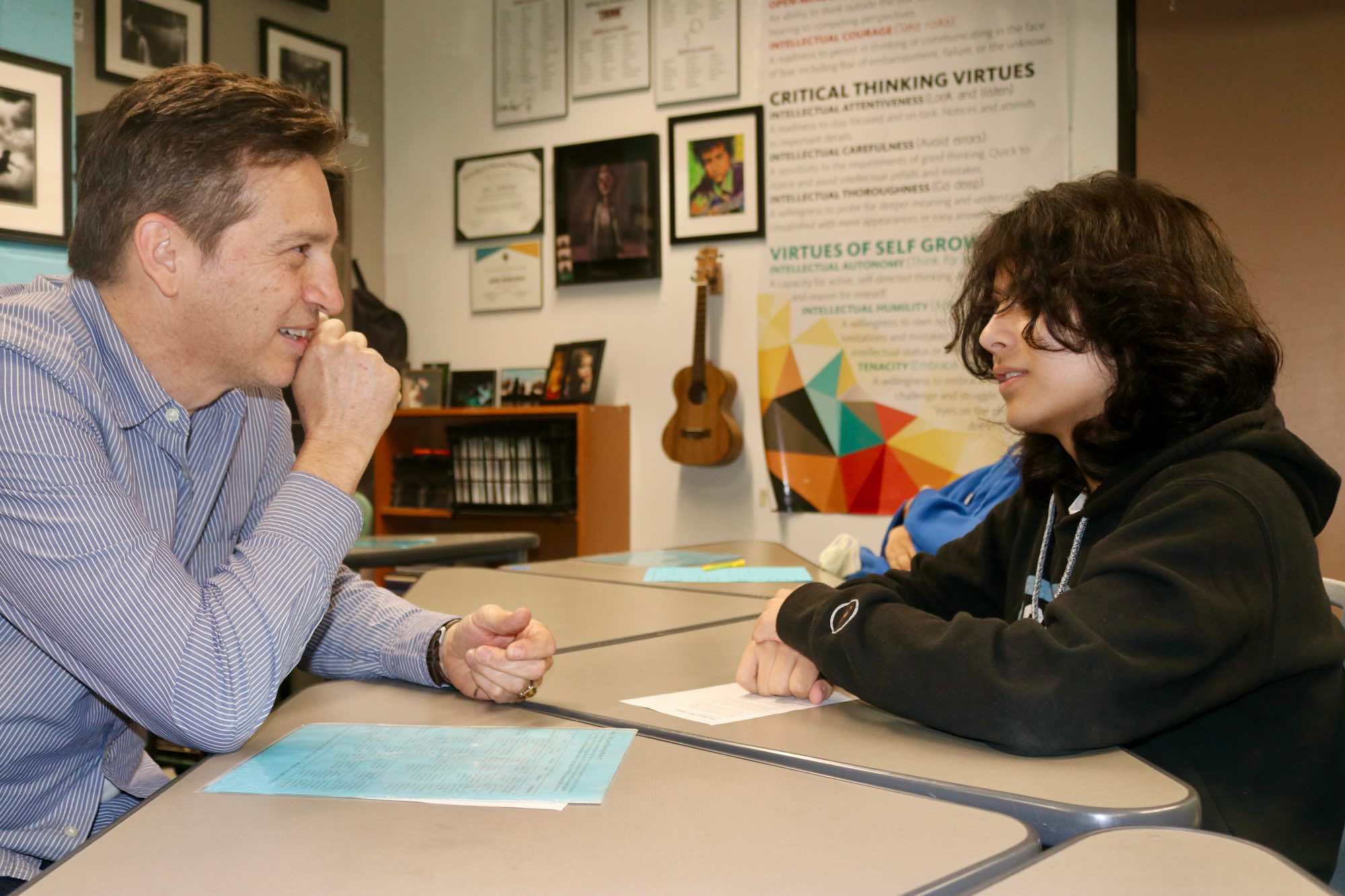 IVA student and teacher sit facing each other at a classroom desk 