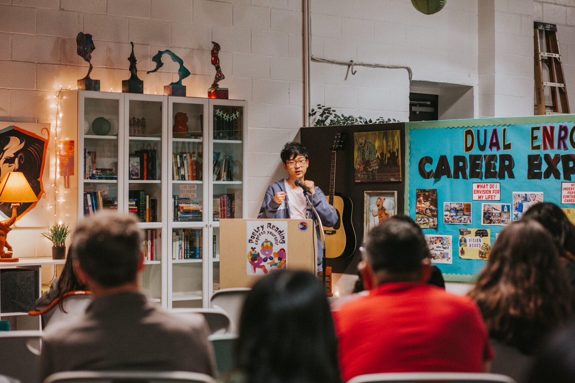 A student at IVA High stands behind a podium and speaks into a microphone while people in the audience listen.