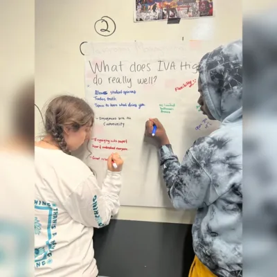 Students at IVA High write on a piece of chart paper hanging on the wall. The prompt on the paper asks “What does IVA High do well?” 