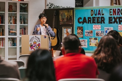 Student speak into microphone at a podium, facing audience members.