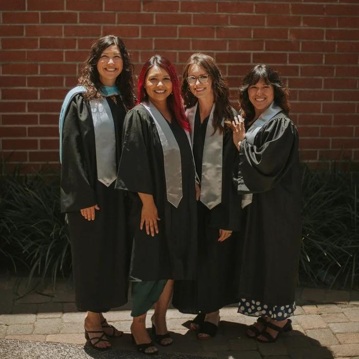 4 people in graduation gowns in front of brick wall