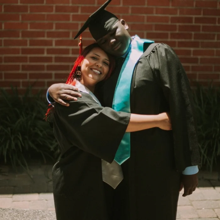 two people in graduation cap and gown hugging