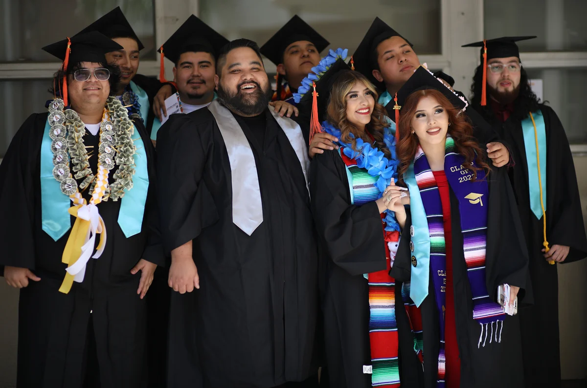 2022 IVA High graduates and faculty pose together for a photo. They are wearing black robes and caps with a variety of colorful stoles.