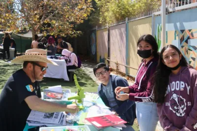 students gather around a table outside in front of a colorful fence