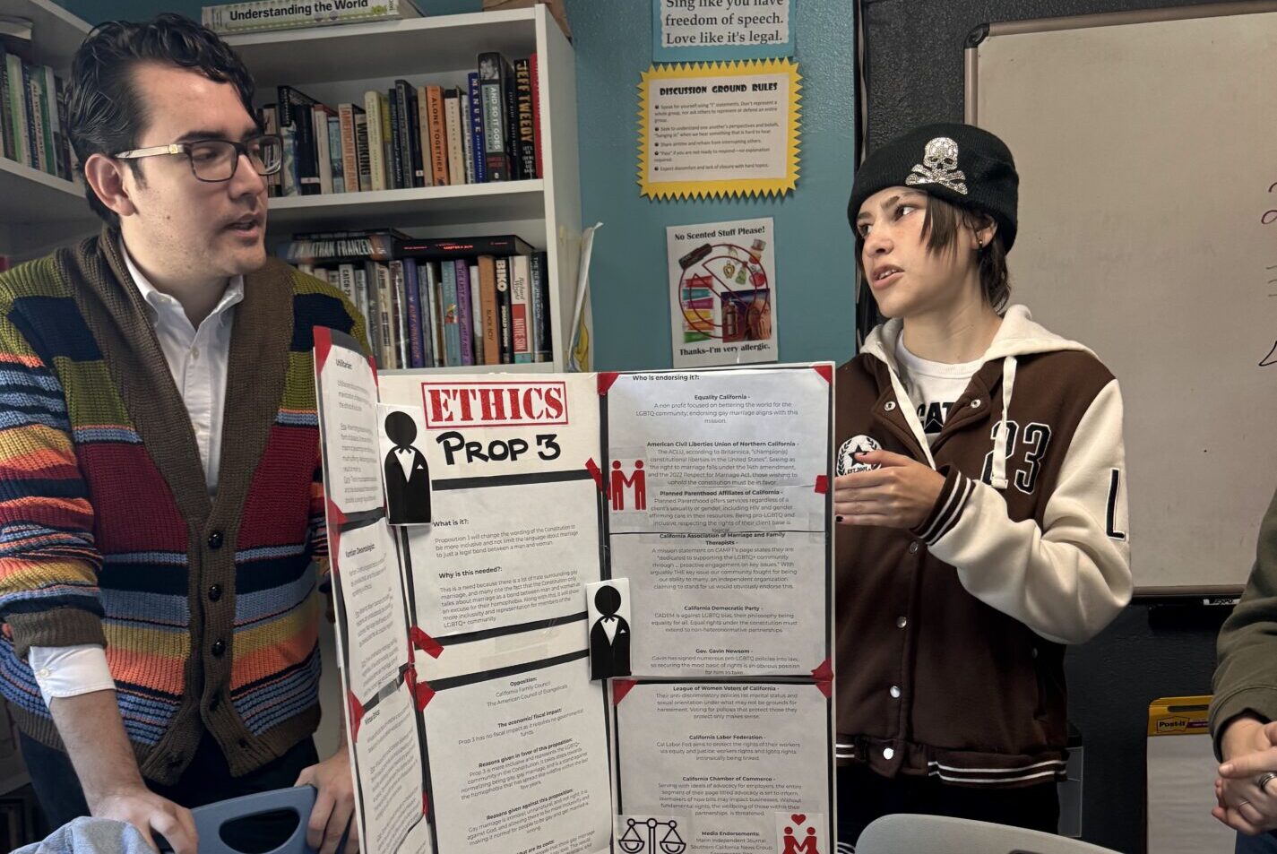 A teacher and student at IVA High stand near a project with the title Ethics in a classroom