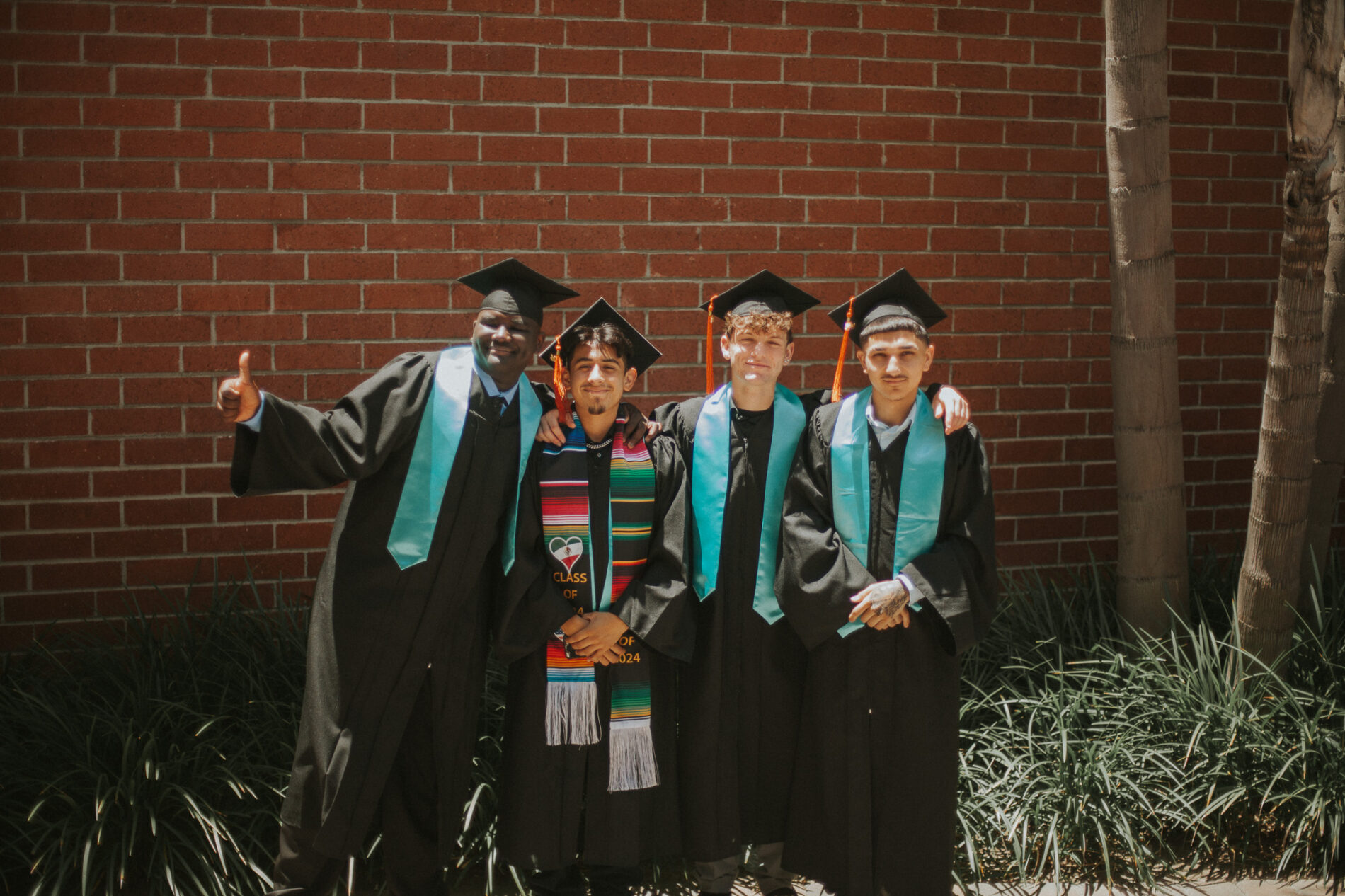 4 graduates of IVA High pose together for a photo. They are wearing graduation caps and gowns and colorful stoles.