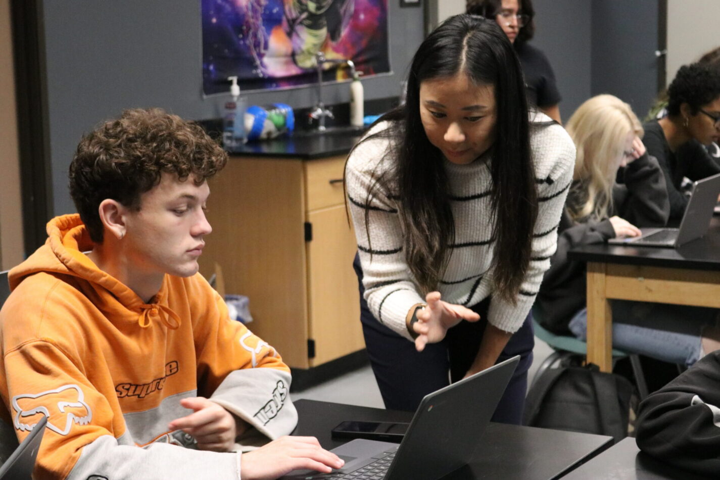 IVA High School student in a classroom collaborating with a teacher and their laptop.